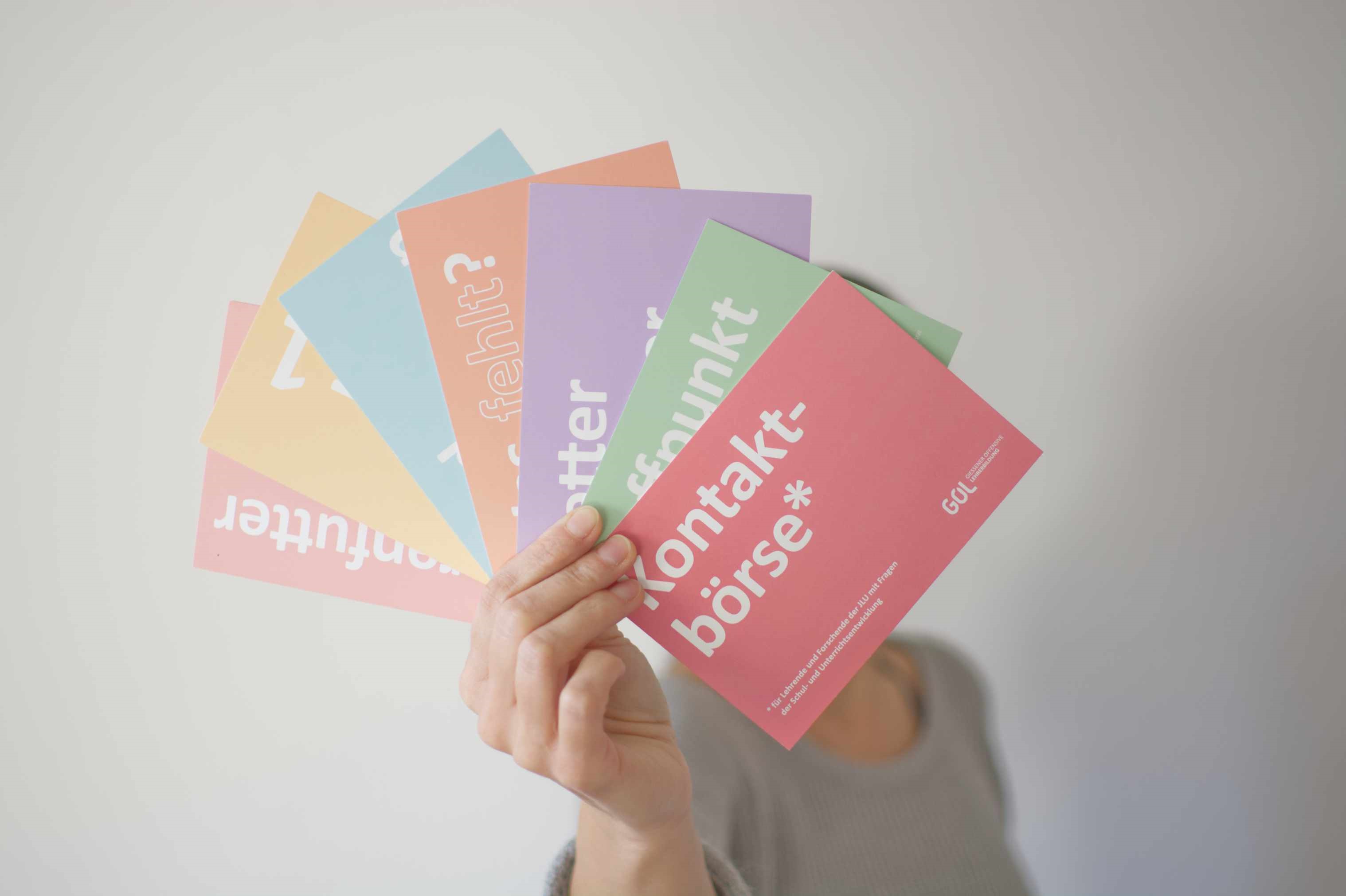 Eine Hand hält aufgefächert bunte Postkarten in die Kamera