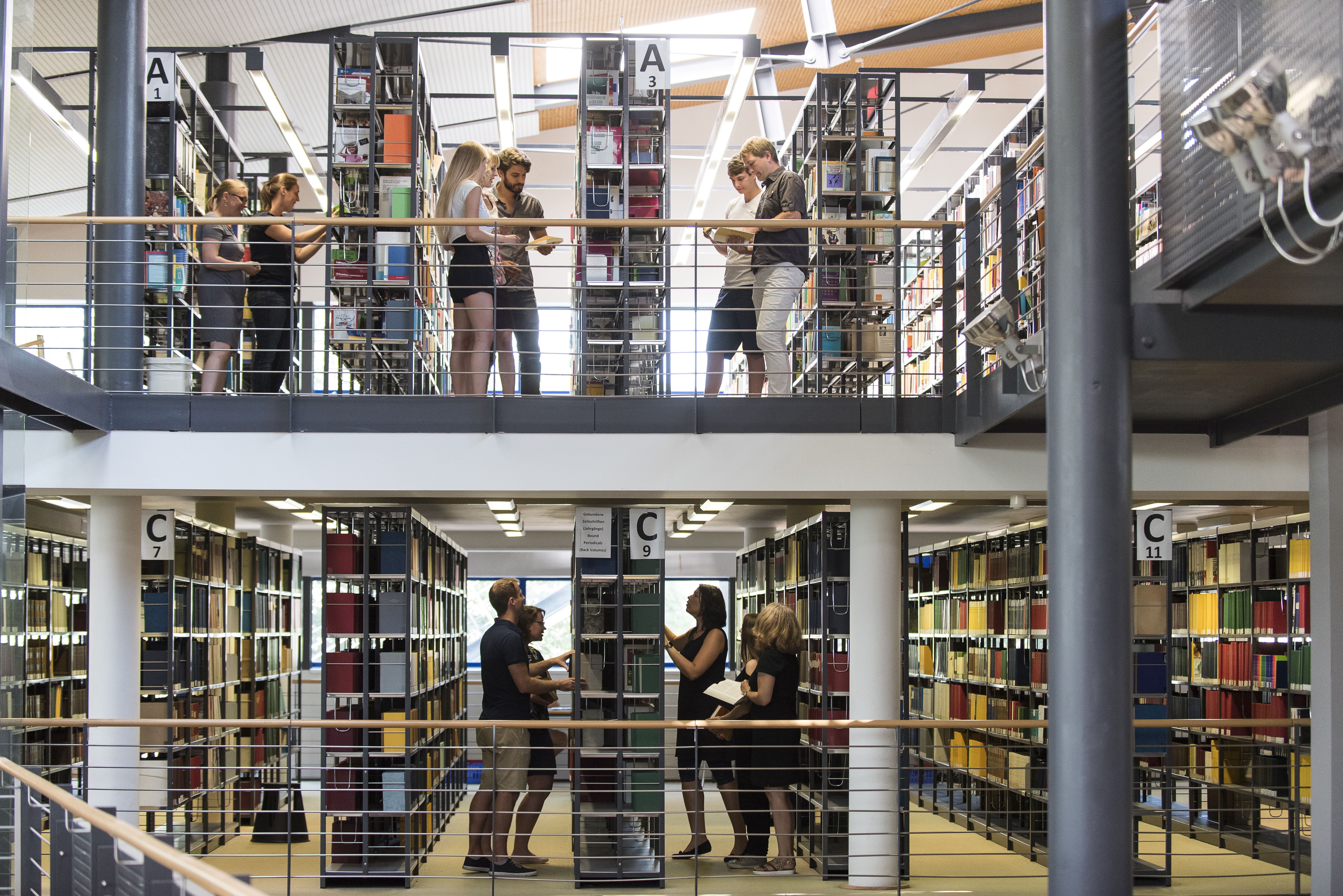 Mehrere Personen stehen zwischen Bücherregalen in einer Bibliothek und betrachten Bücher.