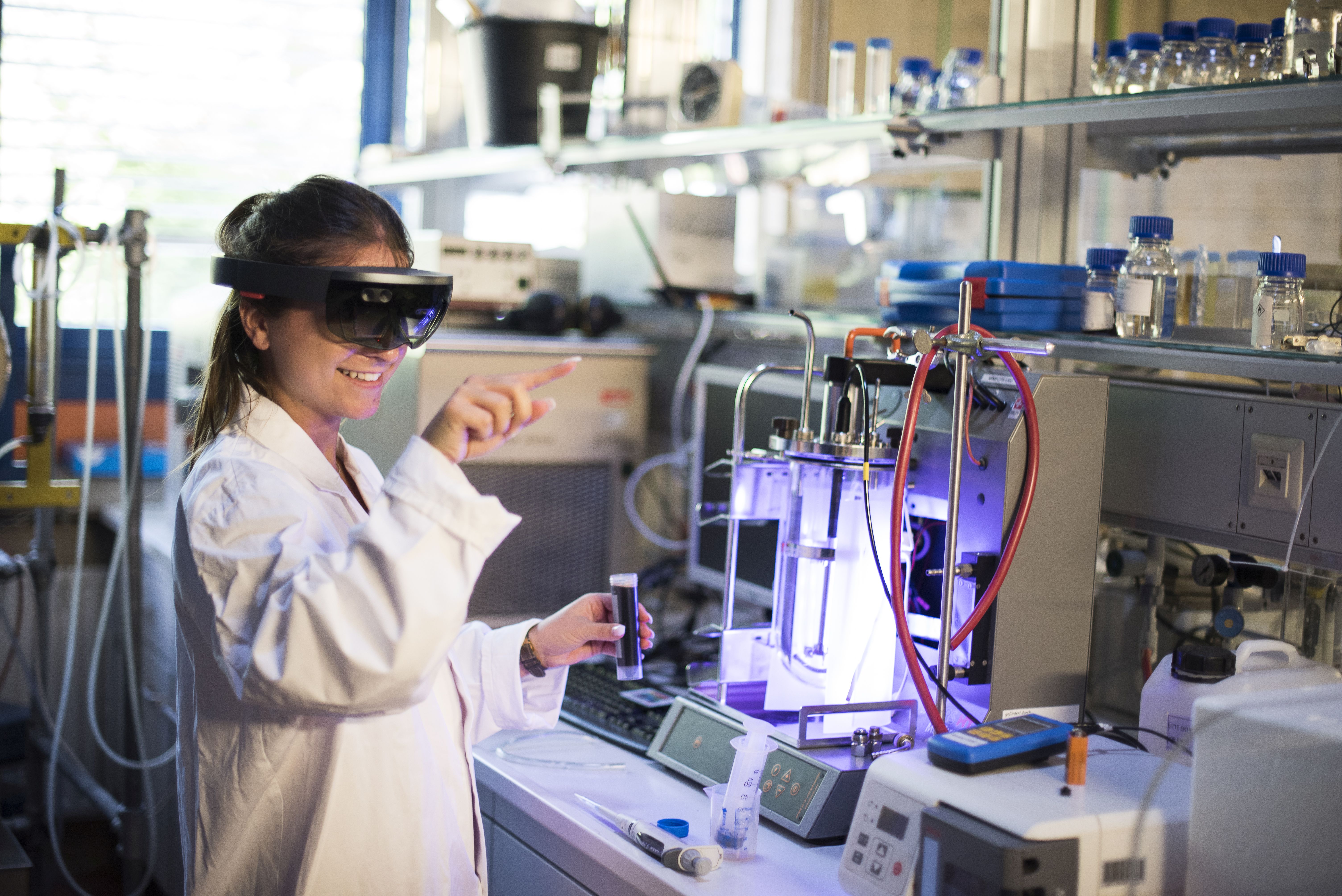 Eine junge Frau arbeitet in einem Labor. Dabei trägt sie eine VR-Brille.