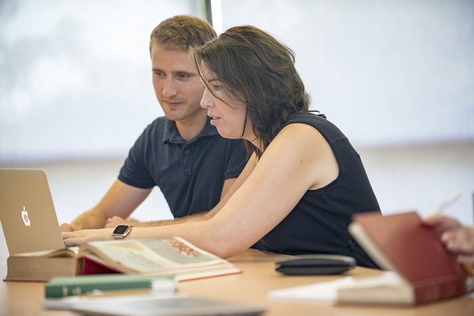 zwei Personen sehen in einen Laptop, um sie herum Bücher