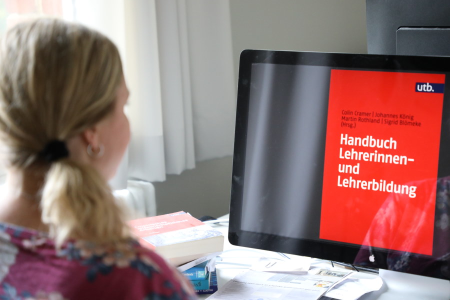 eine Frau blickt auf einen Bildschirm und betrachtet das Cover das Handbuchs Lehrerinnen- und Lehrerbildung