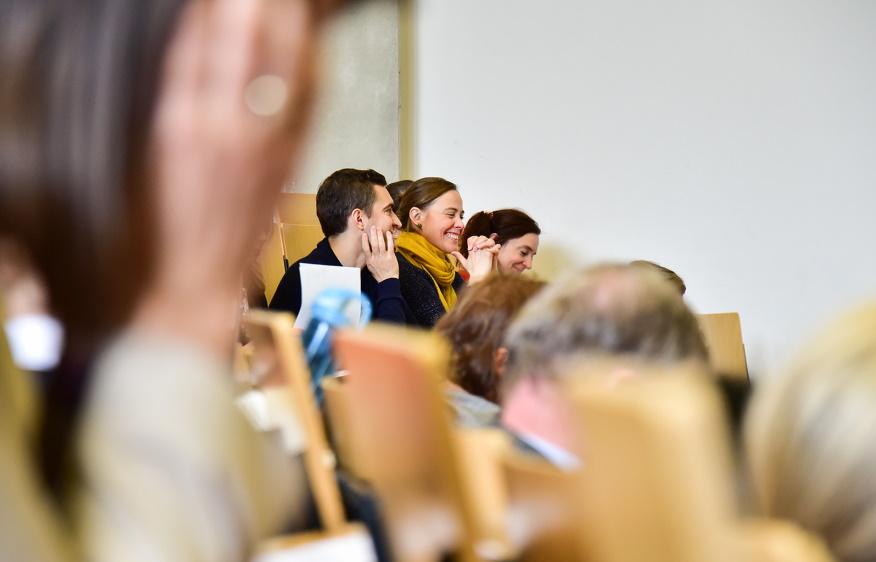 mehrere Menschen sitzen in einem Hörsaal und lachen; © BMBF/Konitzki