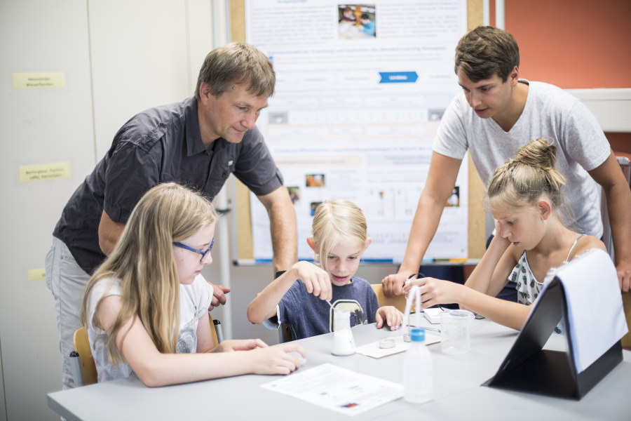 Kinder führen ein Experiment durch und werden von zwei Erwachsenen dabei betreut