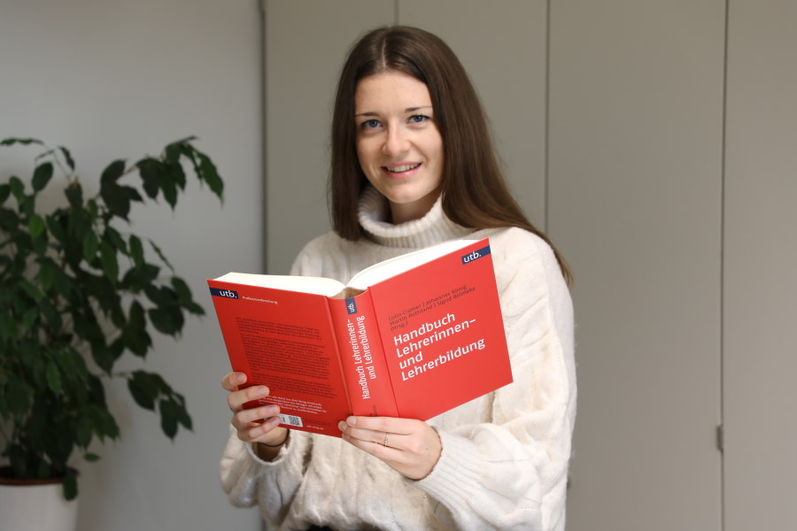 Eine Frau hat ein aufgeschlagenes Buch in der Hand und schaut in die Kamera