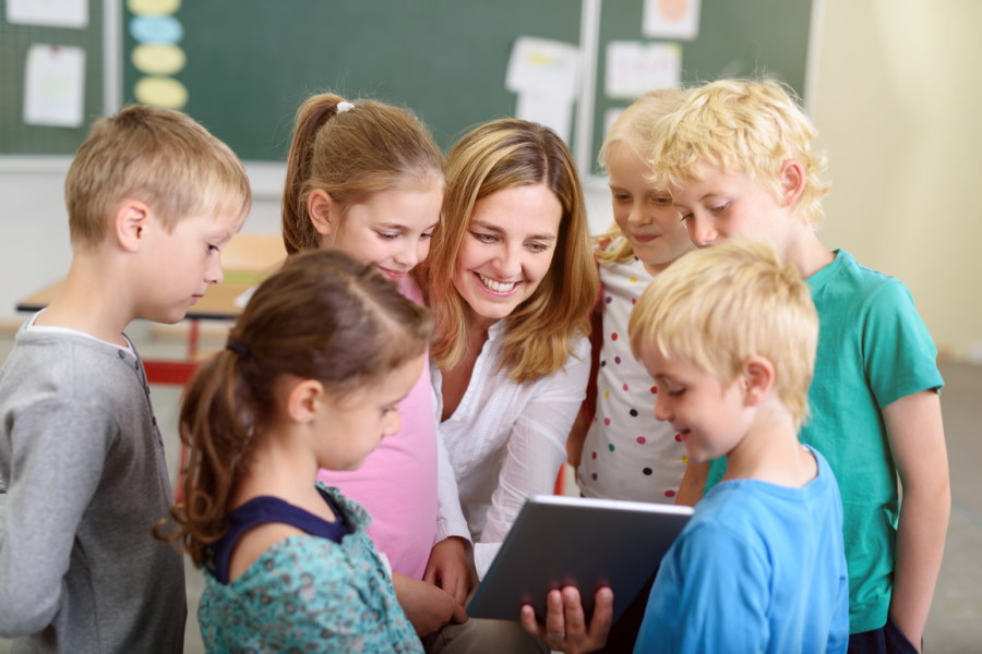 eine Lehrerin zeigt mehreren Schülerinnen und Schüler etwas auf einem Tablet