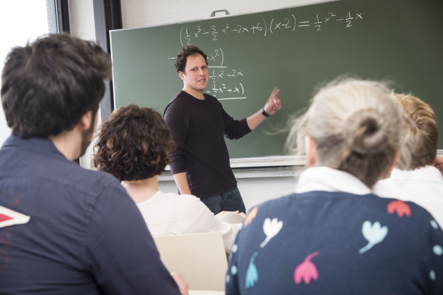 Ein Dozent steht an einer Tafel und erklärt Studierenden im Hörsaal eine mathematische Formel