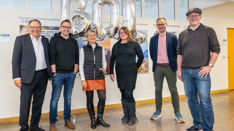 Zwei Frauen und vier Männer stehen vor silbernen Luftballons mit den Buchstaben B, Q und L.