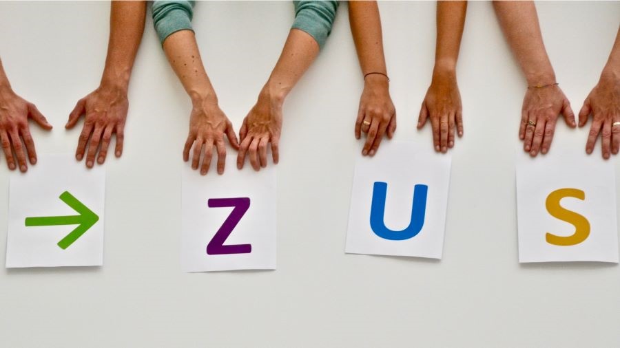 Vier paar Hände weisen auf vier Zettel mit einem grünen Pfeil und dem farbigen Schriftzug Z U S